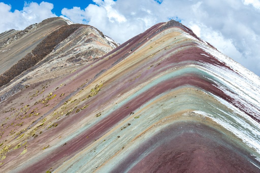 Hikers reaching the summit of Rainbow Mountain with colorful mineral layers in the background