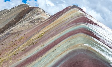 Hikers reaching the summit of Rainbow Mountain with colorful mineral layers in the background