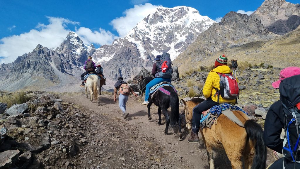 Group of travelers riding horses toward the Ausangate 7 Lagoons with the snow-capped mountain in the background