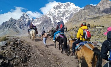 Group of travelers riding horses toward the Ausangate 7 Lagoons with the snow-capped mountain in the background